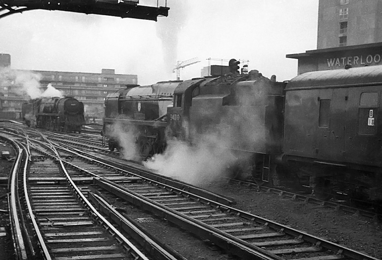 Photo of Bulleid West Country Class pacific number 34010, Sidmouth, waits at the head of a departure from Waterloo as a Bulleid Bulleid Merchant Navy Class pacific reverses out light engine, mid 1960s