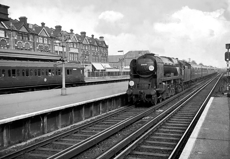 Photo of Bulleid West Country  Class pacific number 34101, Hartland, drifting into the Woking stop past an up BIls train, when working a London, Waterlooo to Bournemouth train in the mid 1960s
