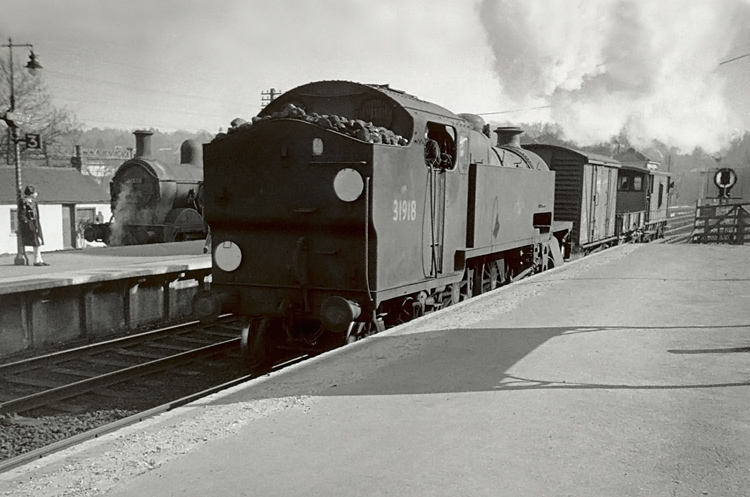 Photo of W Class 2-6-4 tank loco 31918 on a short goods train passing H Class 0-4-4-0 tank loco 31551 on a push pull train in the bay platform at Oxted. Spring 1962